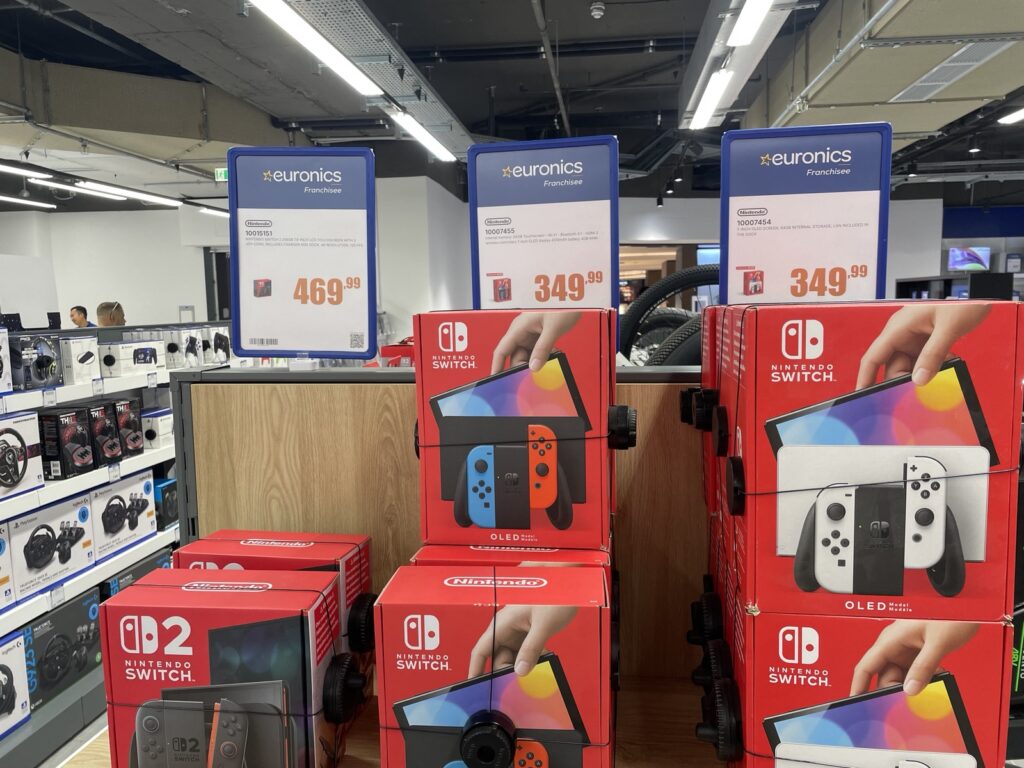 An image of the original nintendo switch and the switch 2 in a retail store with old pricing